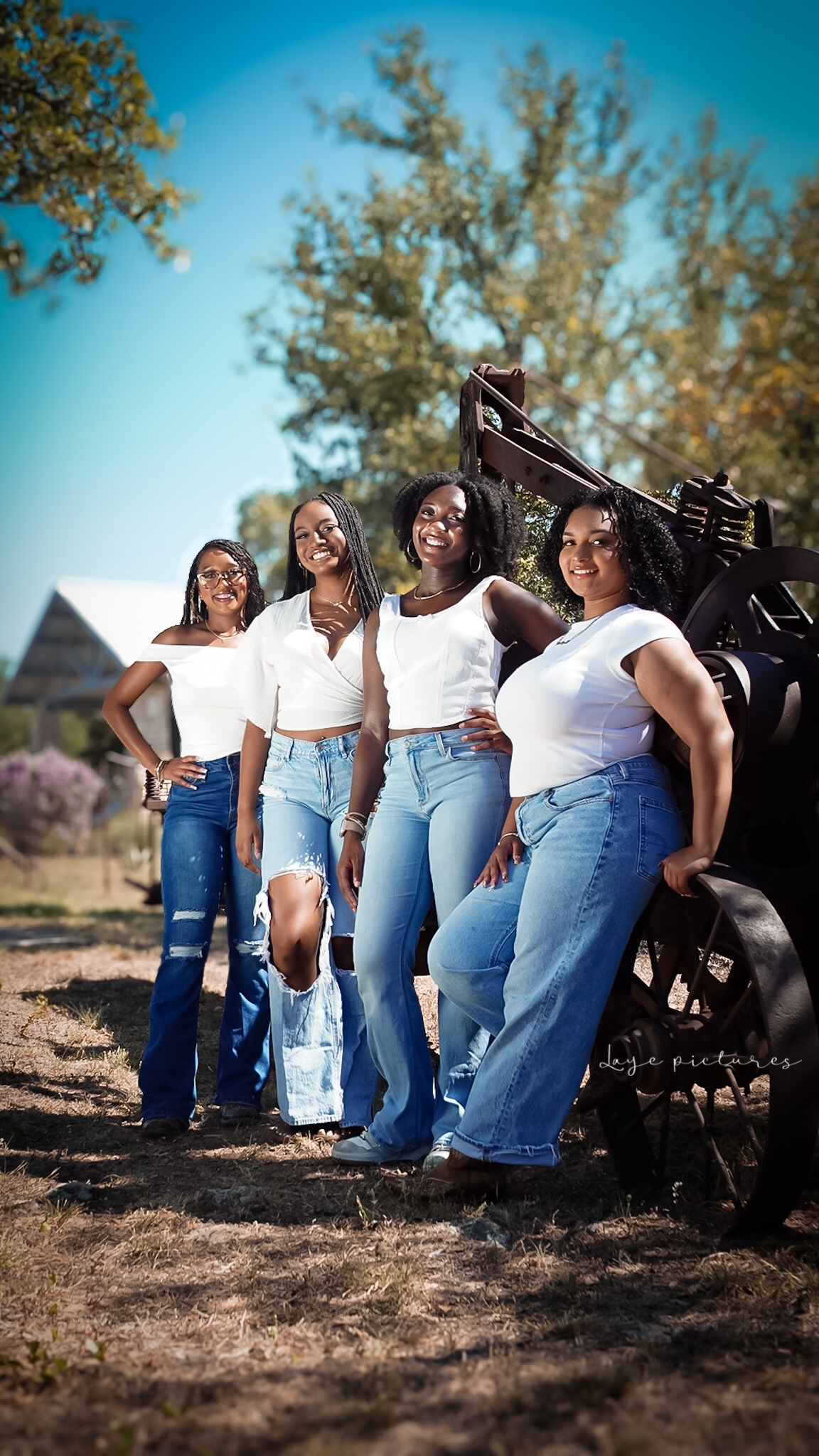 Four women posing outdoors in white tops and blue denim